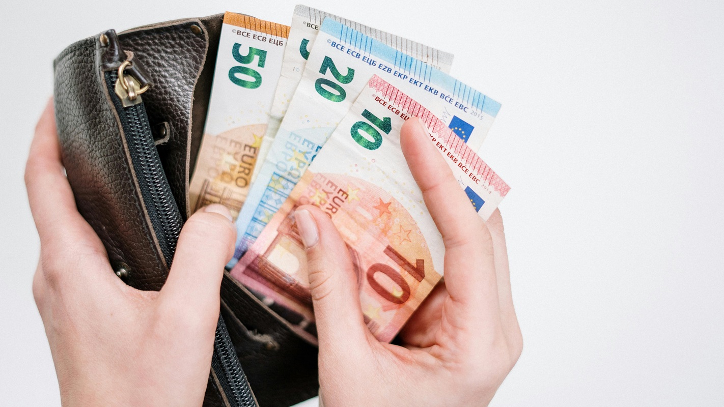 Detailní záběr na ruce vytahující bankovky z hnědé peněženky